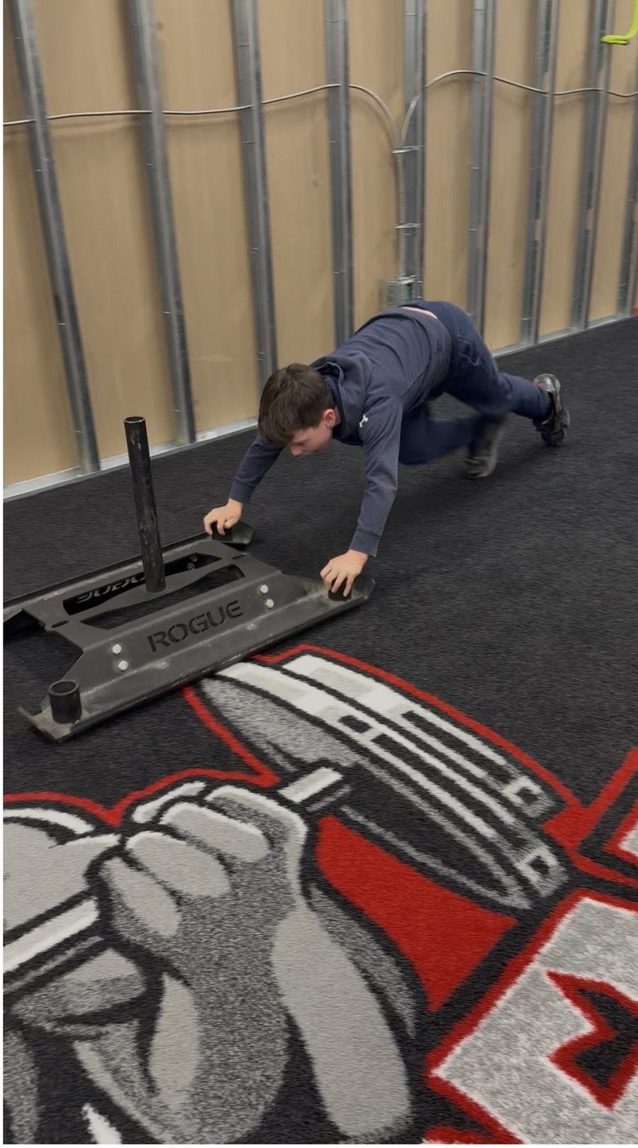 Athlete driving a weighted sled across the Rhino Den turf floor